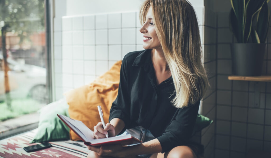 a pretty girl writing beside a window
