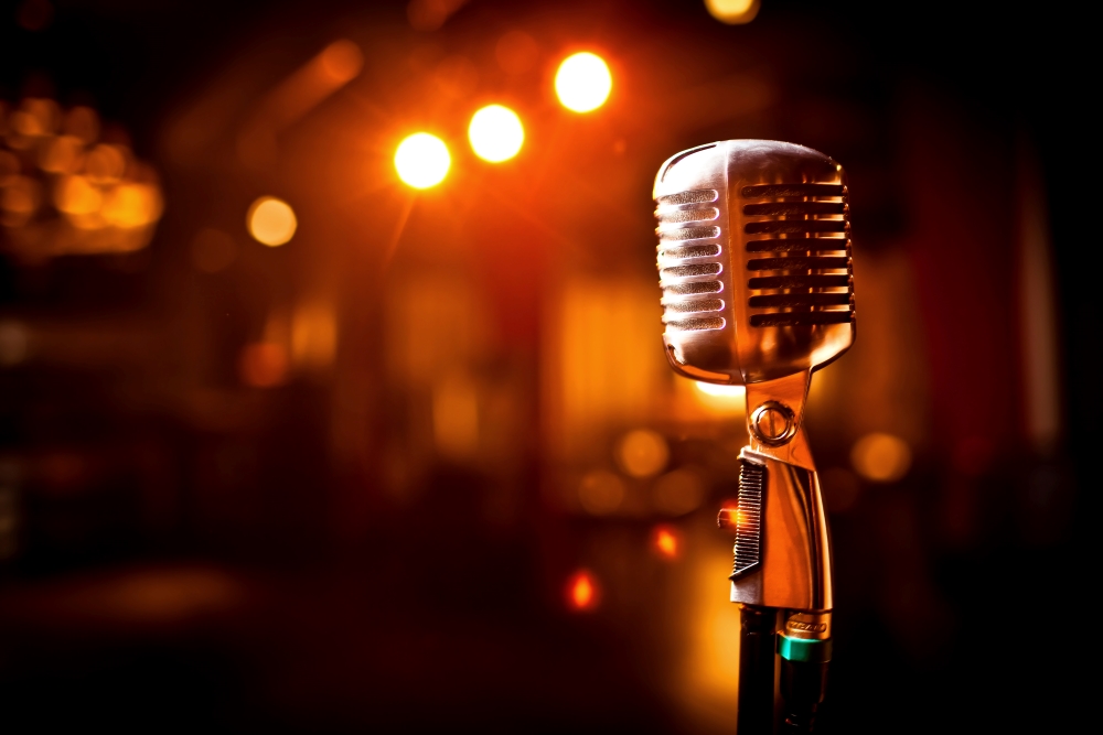 A nickel plated old fashioned microphone on a stand, with low club lights in the background